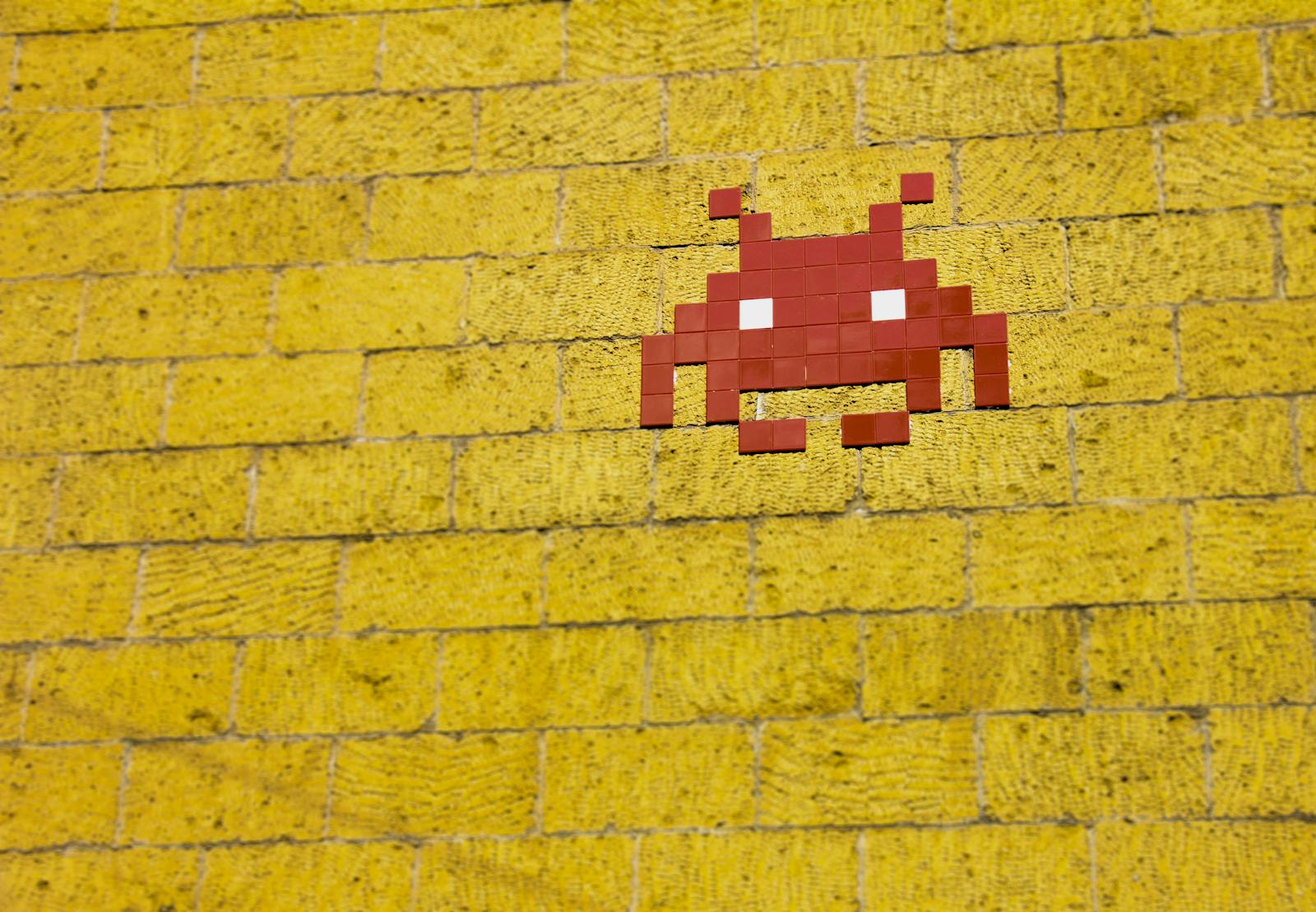 Street art of a space invader. Street art featuring a retro pixelated space invader on a vivid yellow brick wall.