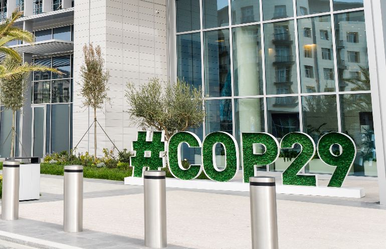 A photo of COP29 in Baku. A photo showing a large sign that reads "#COP29" outside of a building largely composed of windows.