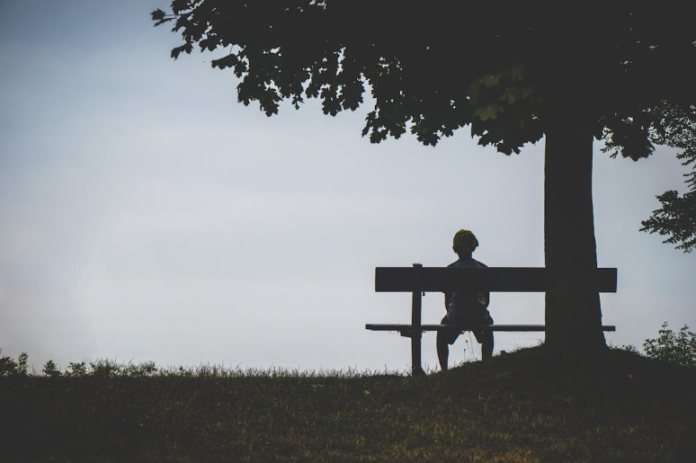 The outline of a child sitting on a bench in gloomy weather, looking into the distance.