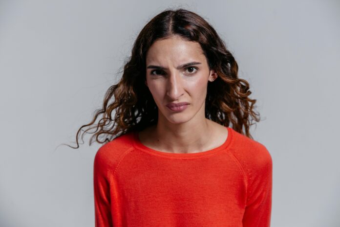 A woman wearing an orange jumper looking unimpressed.
