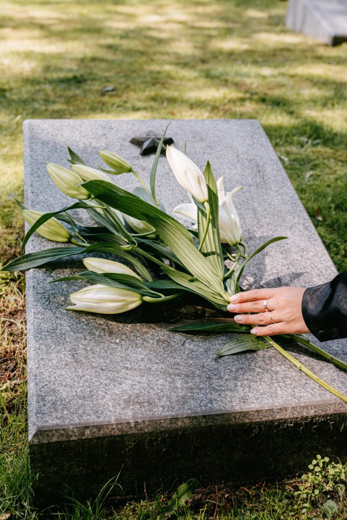 A hand lays a bouquet of white flowers on a grave stone.