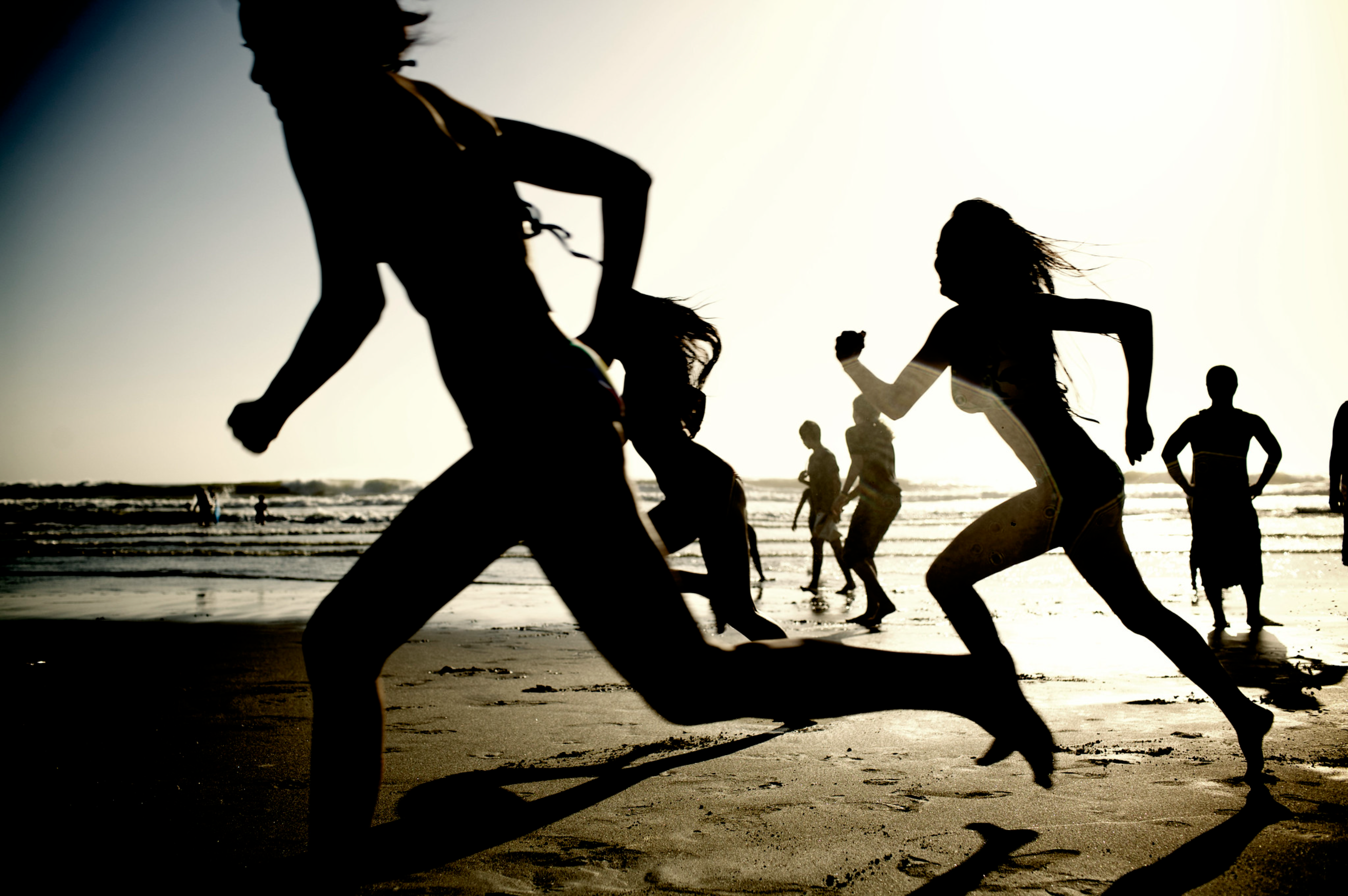 People running along a beach. People running on the beach with the sun behind them.
