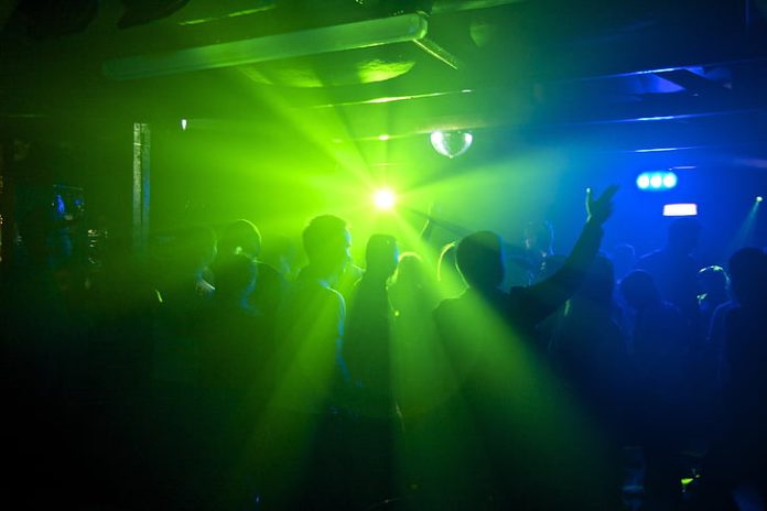 A photo of a crowd of people dancing in a club with green and blue lighting.