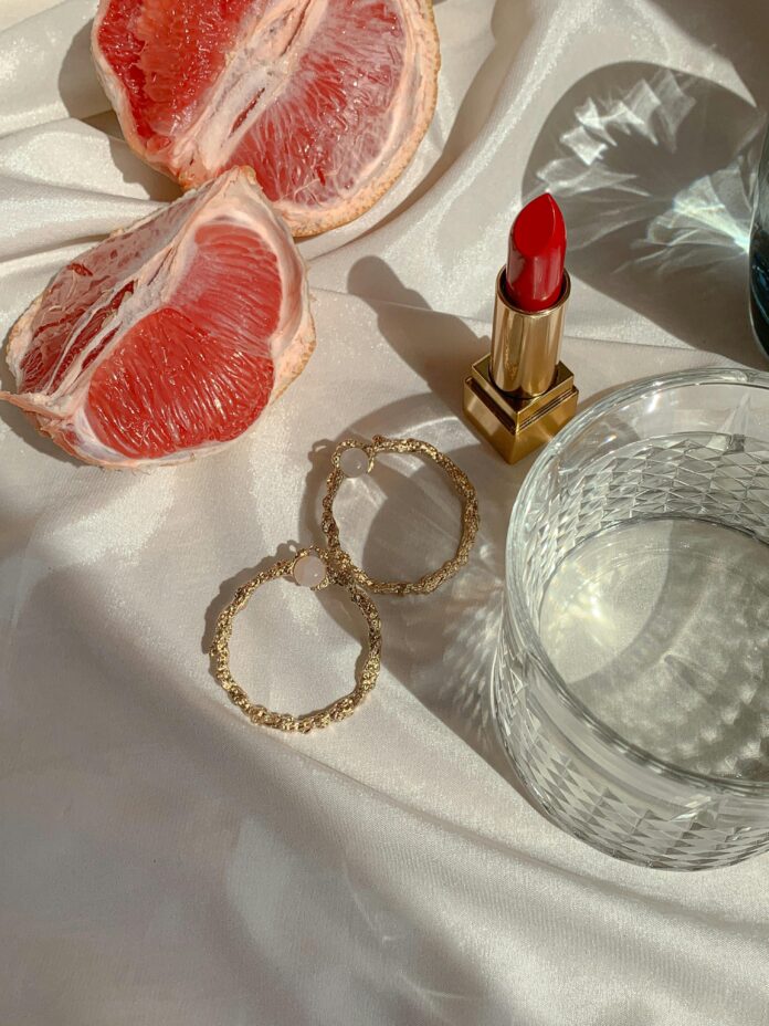 Red lipstick, hoop earrings and blood orange next to whiskey glass.