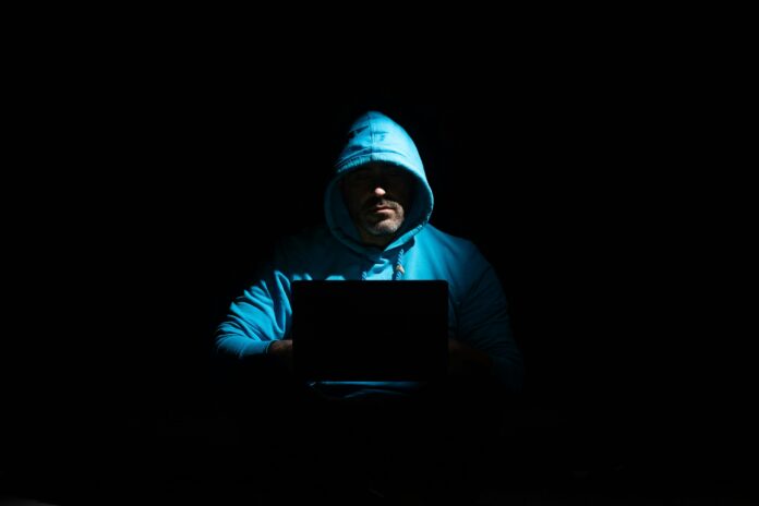Person in blue hoodie sitting in the dark with a laptop.