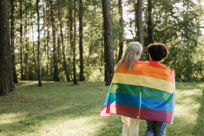 Women in the woods draped in pride flag from behind