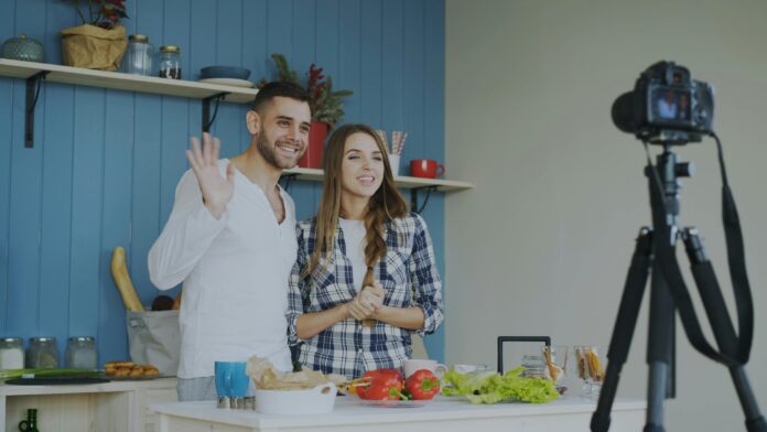 Couple filming cooking video in kitchen with camera on tripod